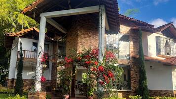 Une maison à deux étages avec une façade en briques, un balcon en bois et un jardin agrémenté de plantes en pot et de fleurs.