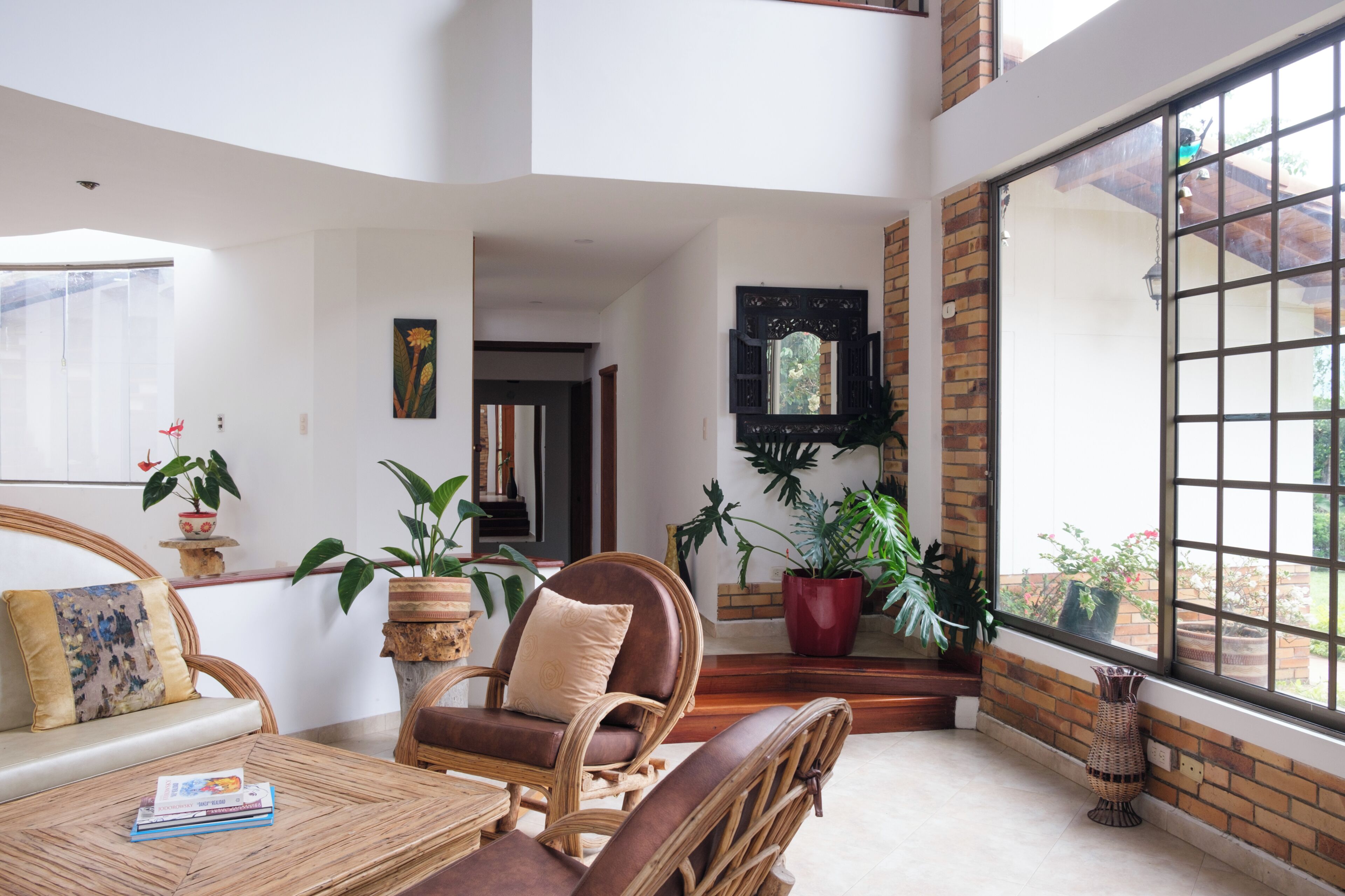 A spacious room with a large window, wicker furniture, and potted plants.
