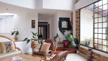 A spacious room with a large window, wicker furniture, and potted plants.