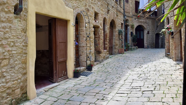 Uma rua de paralelepípedos com edifícios de pedra, portas de madeira e janelas em arco.
