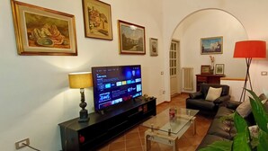 Uma sala de estar com televisão, sofá, mesa de centro e diversas fotos emolduradas na parede.