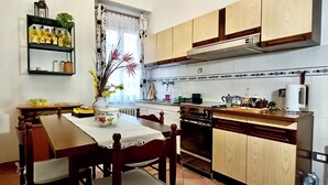 Cozinha compacta com armários de madeira, mesa de jantar com cadeiras, um vaso com flores e uma estante com garrafas.