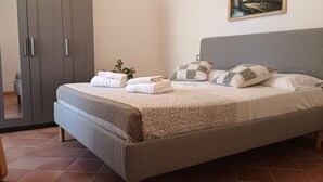Quarto com cama, almofadas, uma planta na mesa de cabeceira e uma cadeira.