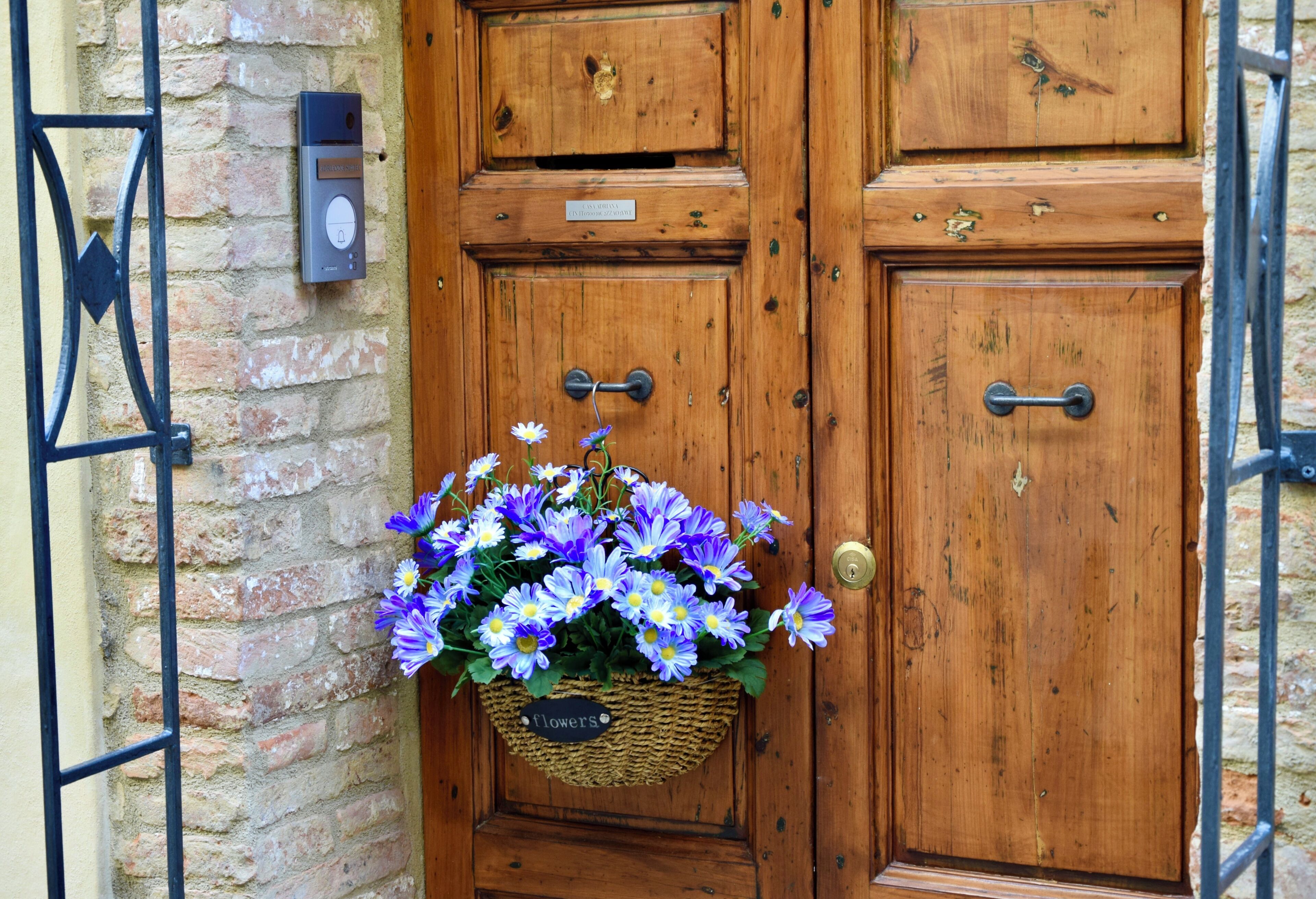 A wooden door with a metal gate, a brick wall, and a basket of flowers.