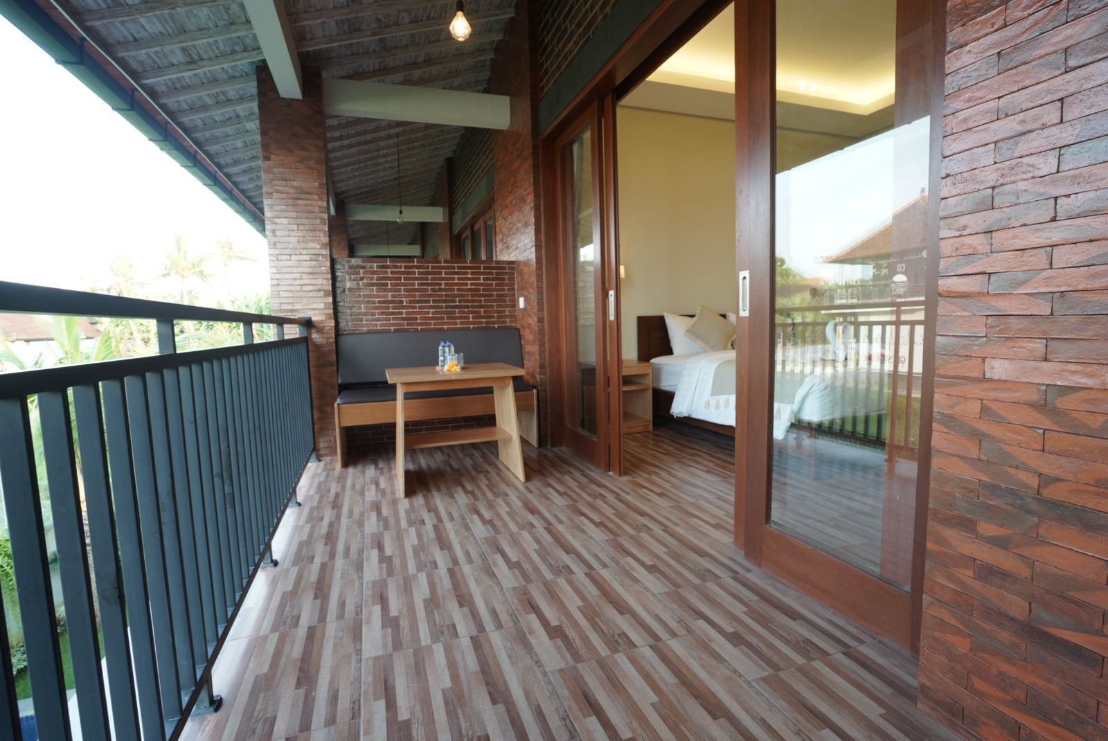 Ein Balkon mit Holztisch und Bank, ein Bett mit weißer Bettwäsche sowie eine Backsteinwand.