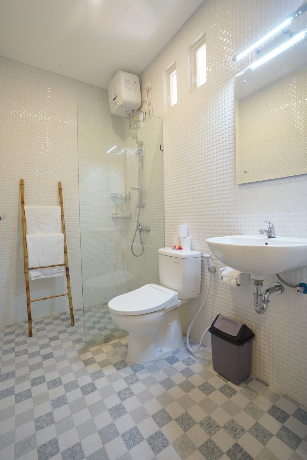 Une salle de bain comprenant des toilettes, une douche et un lavabo, ainsi qu’un carrelage au motif à carreaux et un porte-serviettes.