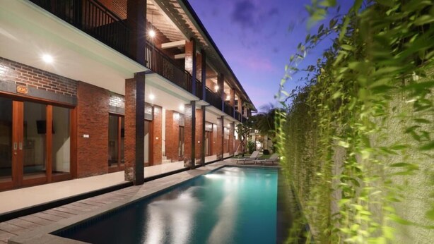 A modern hotel with a swimming pool, multiple balconies, and a brick facade. - Sunkiest House Canggu (Tibubeneng)