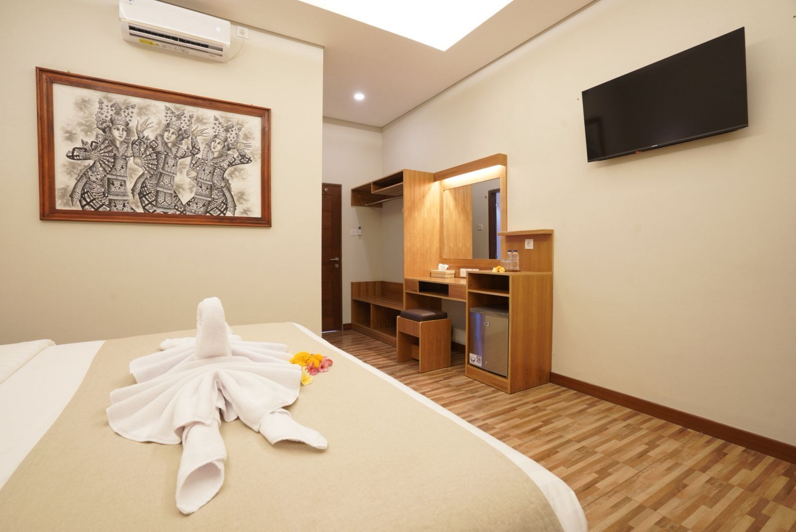 A hotel room with a bed, a painting, a TV, a mirror, and a wooden cabinet.