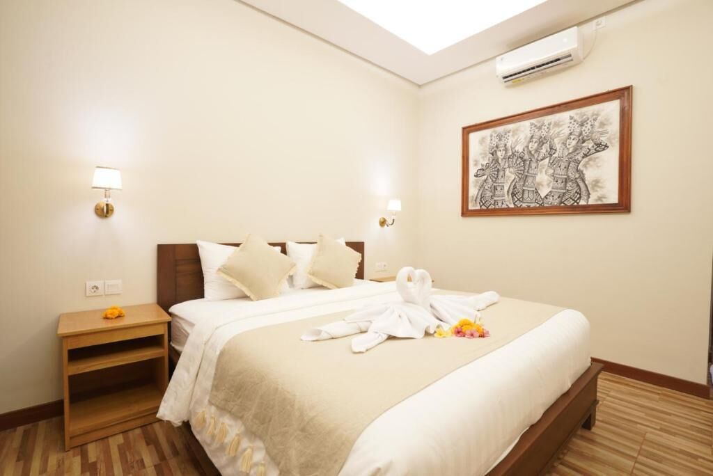 A hotel room with a bed, bedside tables, a wall-mounted air conditioner, and a framed artwork.