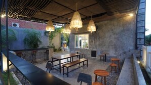 An outdoor seating area with tables and benches, a bar, and hanging lights. - Sunkiest House Canggu (Tibubeneng)