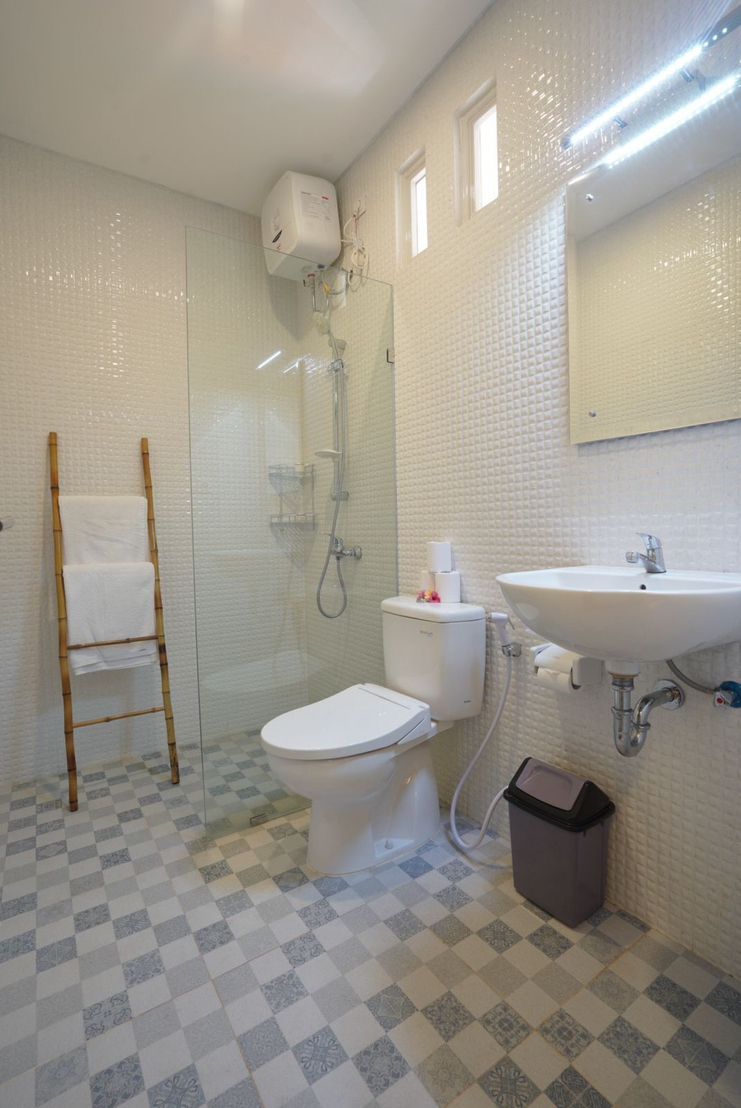 A bathroom with a glass shower enclosure, a toilet, a sink, and a checkered floor pattern.