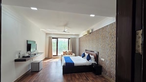 A hotel room with a bed, a desk, a television, and a sliding door to a balcony. - Posh Classic, sector 45, millenium city centre, gurugram (Gurugram)