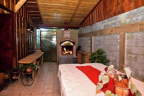 A rustic room with a brick fireplace, wooden beams, a bed with a red blanket, and potted plants. - Santa Ana City Views Chalet (Pabellón)