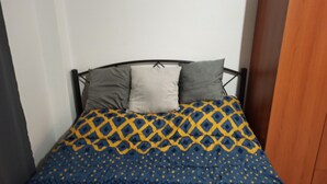 A bed with a patterned blue and yellow bedspread, two pillows, and a wooden wardrobe in the background. - studio heart of city , Electric Scouter (Thessaloniki city)
