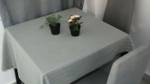 A dining table with a light green tablecloth, two potted plants, and a grey upholstered chair. - studio heart of city , Electric Scouter (Thessaloniki city)