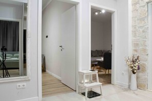 Ein modernes Interieur mit einer weißen Tür, einem kleinen weißen Hocker, einer schwarzen Waage und einer Vase mit Trockenblumen.