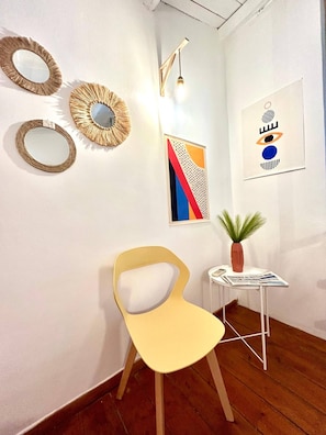 A room with a wooden floor, a yellow chair, a small white table with a magazine, a potted plant, and wall art including mirrors and abstract paintings. - La Casa del Teatro Politeama (Palermo)