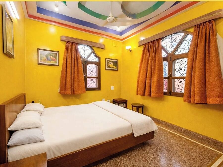 A hotel room with a bed, two bedside tables, a ceiling fan, and two windows with curtains.