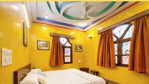 A hotel room with a bed, two windows with curtains, a ceiling fan, and wall-mounted lights.