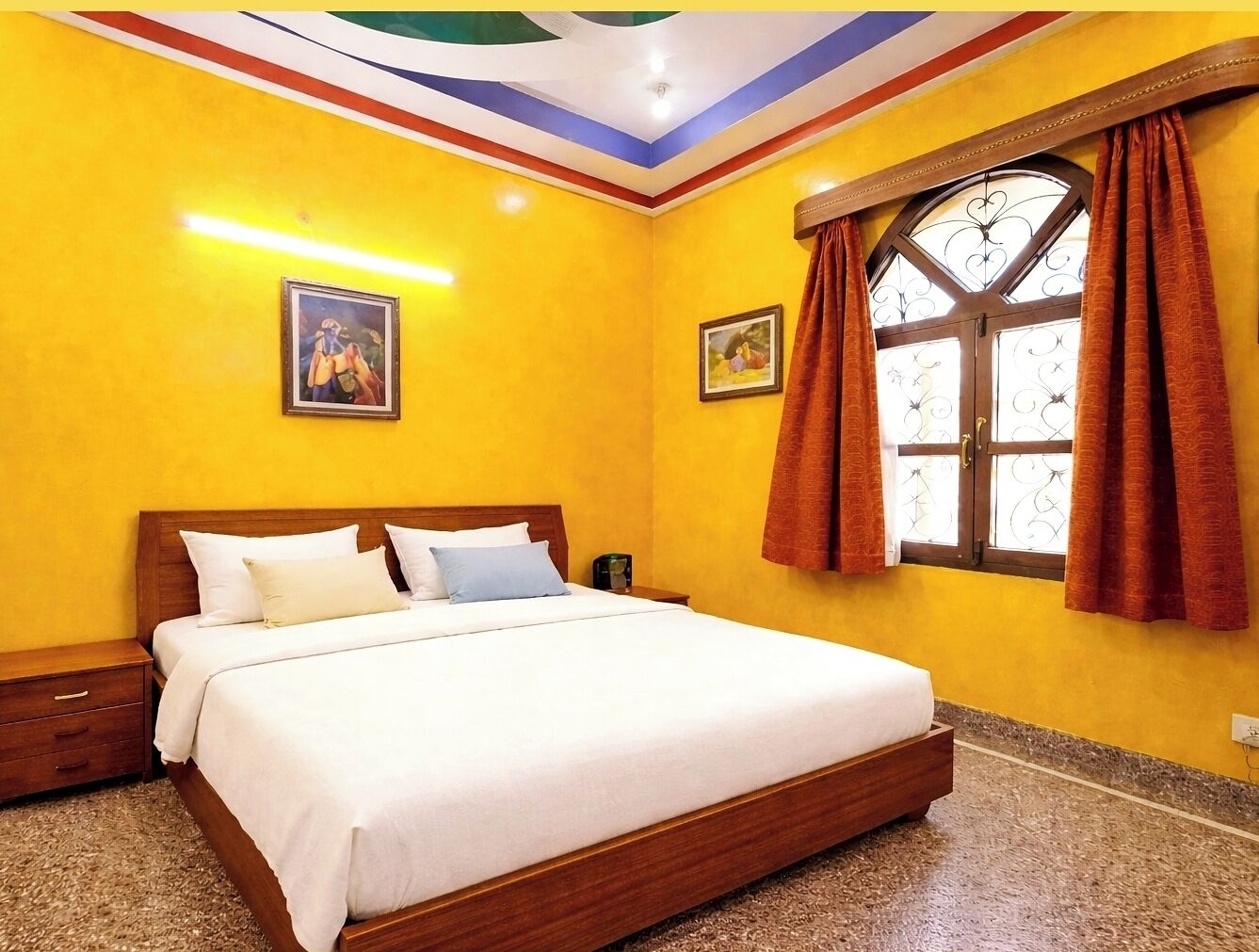 A hotel room with a bed, a nightstand, a window with curtains, and a ceiling with a decorative design.