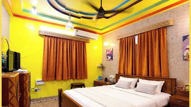 A room with a bed, curtains, a ceiling fan, an air conditioner, a TV, and a wooden dresser.