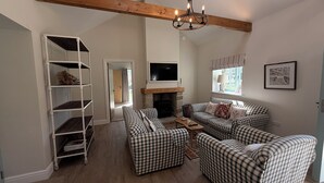 Ein Wohnzimmer mit Kamin, karierten Sofas, einem Fernseher und einem Holzbalken an der Decke.