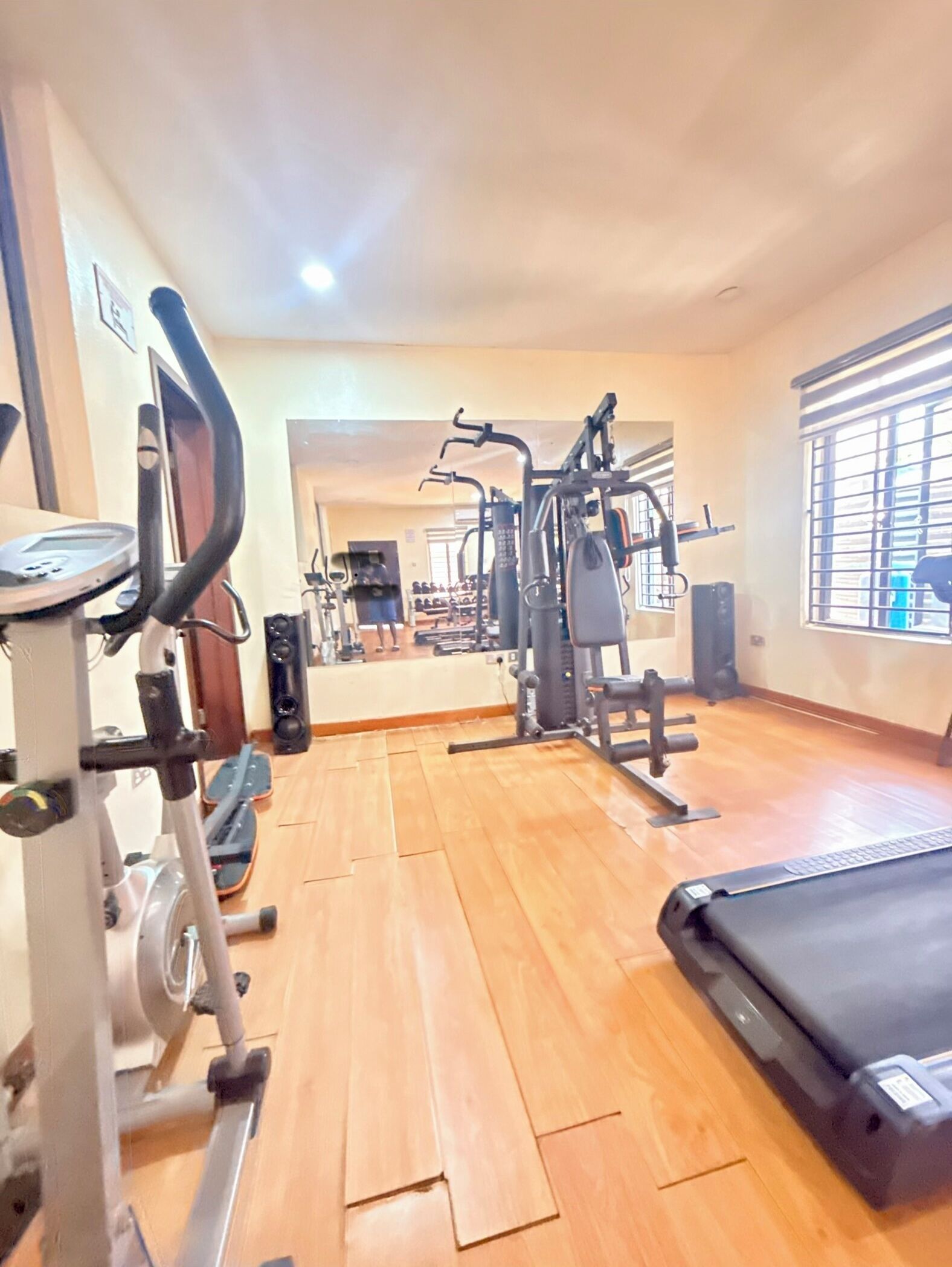 Un gimnasio con equipo de ejercicio, una cinta de correr y un espejo que refleja la sala.