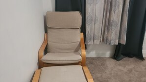 Ein Zimmer mit einem beigefarbenen Sessel, einem weißen Gerät auf dem Boden und einem Teppichboden.
