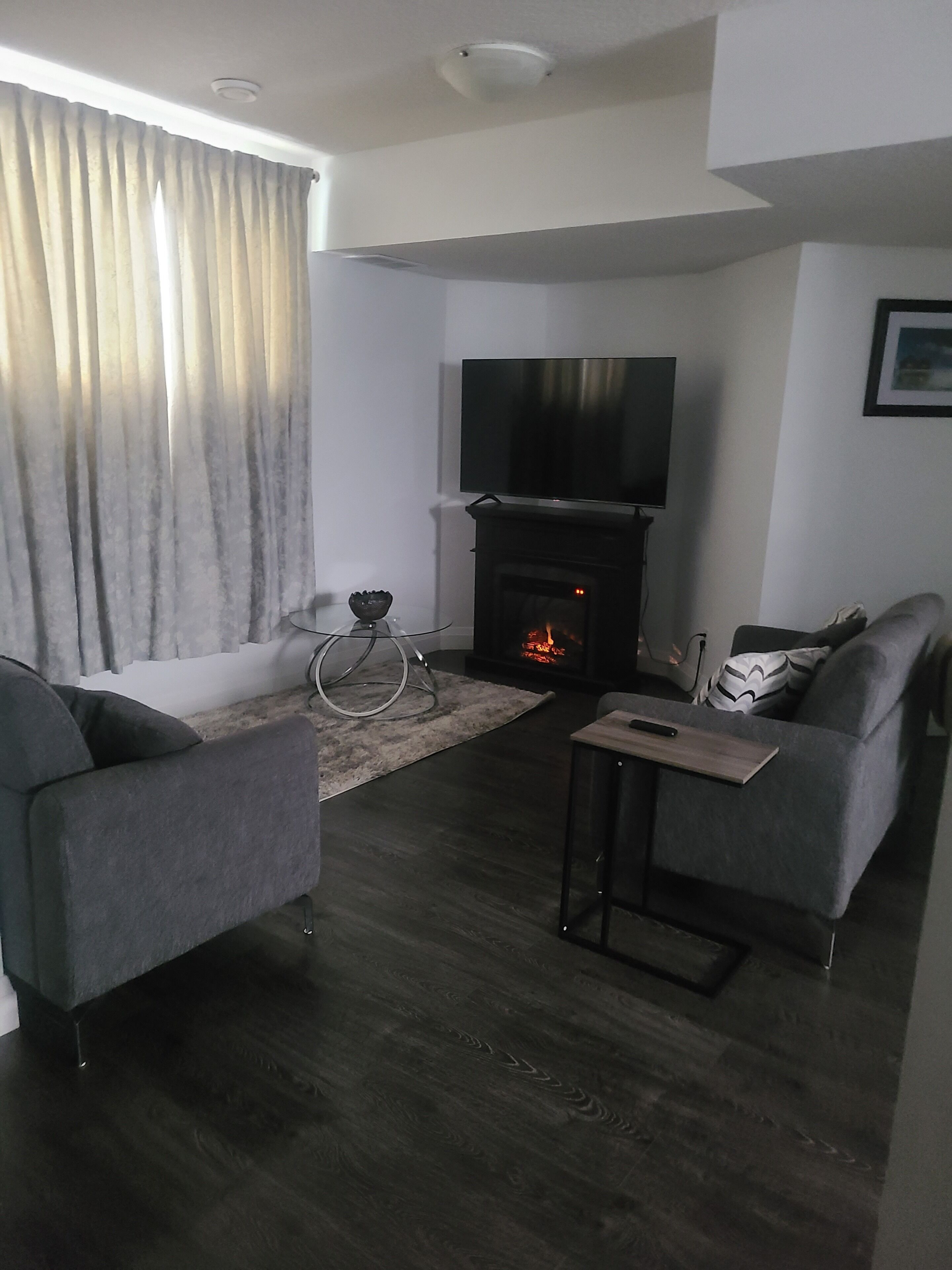 Un salon moderne avec une cheminée, un téléviseur à écran plat et deux fauteuils gris.