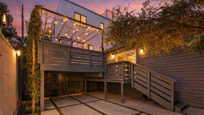 Een modern buiten terras met een houten dek, een kleine trap en lichtslingers.