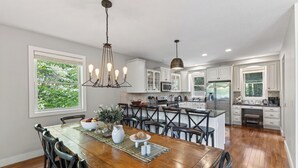 Uma cozinha moderna com armários brancos, uma mesa de jantar de madeira e um candelabro.