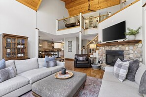 Ein geräumiges Wohnzimmer mit hohen Decken, einem Kamin, einem Fernseher und einer Treppe, die in eine obere Etage führt.