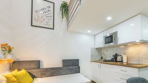 Ein modernes, kompaktes Wohnzimmer mit Sofa, einer kleinen Küchenzeile und einem gerahmten Schild an der Wand.