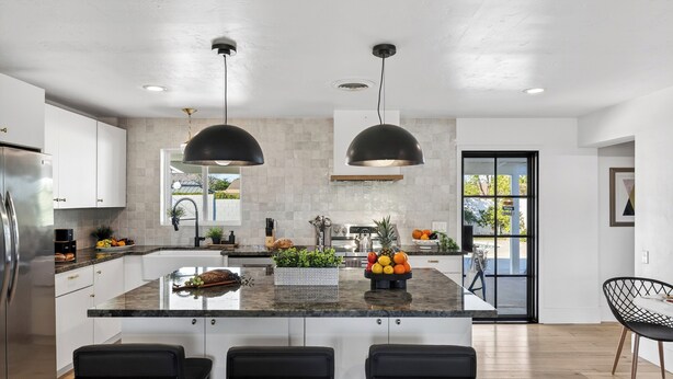 A modern kitchen with a central island, black pendant lights, and a view to the outside. - Private Pool + Firepit + Ping Pong + Expansive Backyard | Mins to Dining (Scottsdale)