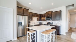 A modern kitchen with dark wood cabinets, stainless steel appliances, and a white island with bar stools. - 4 Mi to Boardwalk! Bethany Beach Getaway (Millville)