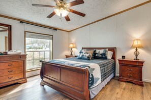 A bedroom with a wooden bed, two bedside tables with lamps, a ceiling fan, and a large window. - Long-Range Mtn Views! Scenic Asheville Sanctuary (Asheville)