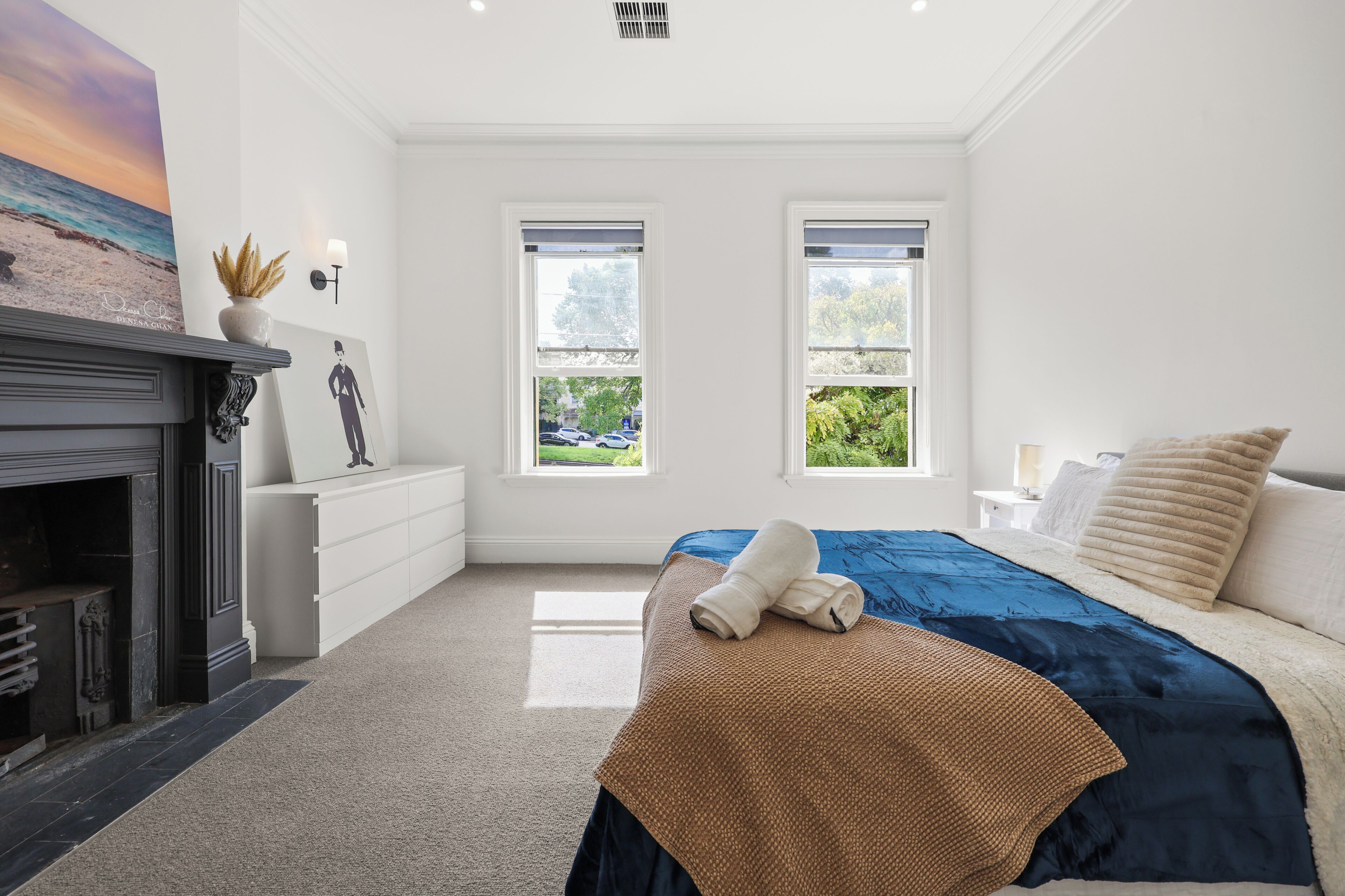 A bedroom with a bed, a fireplace, two windows, and a view of the outdoors.