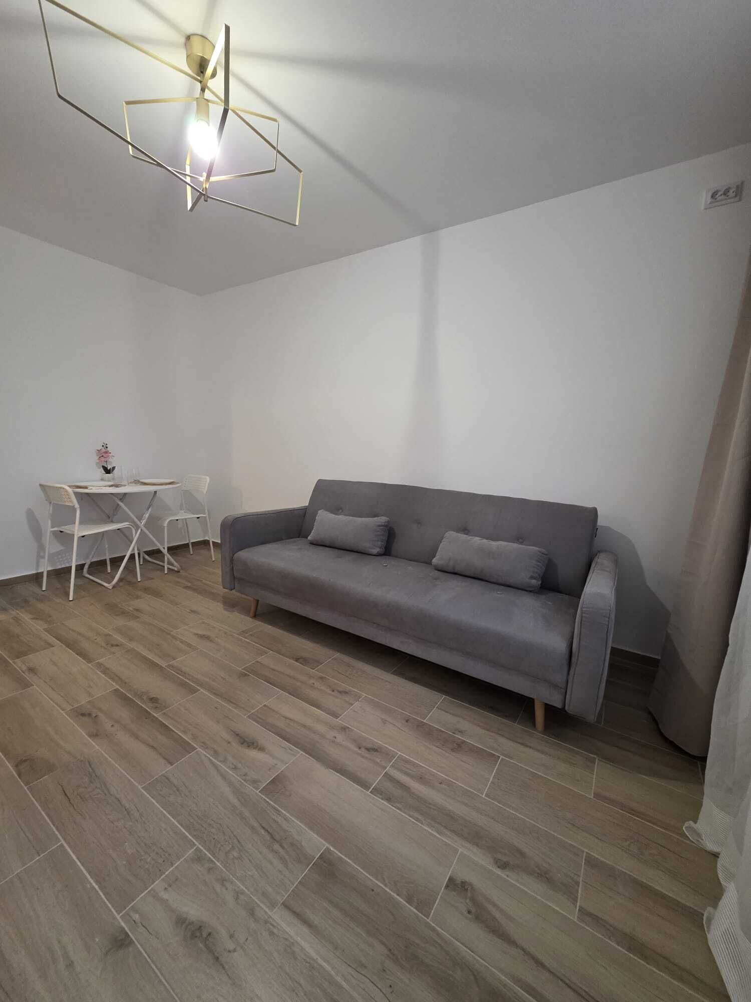 A modern living room with a grey sofa, a small white table with chairs, and a geometric ceiling light fixture.