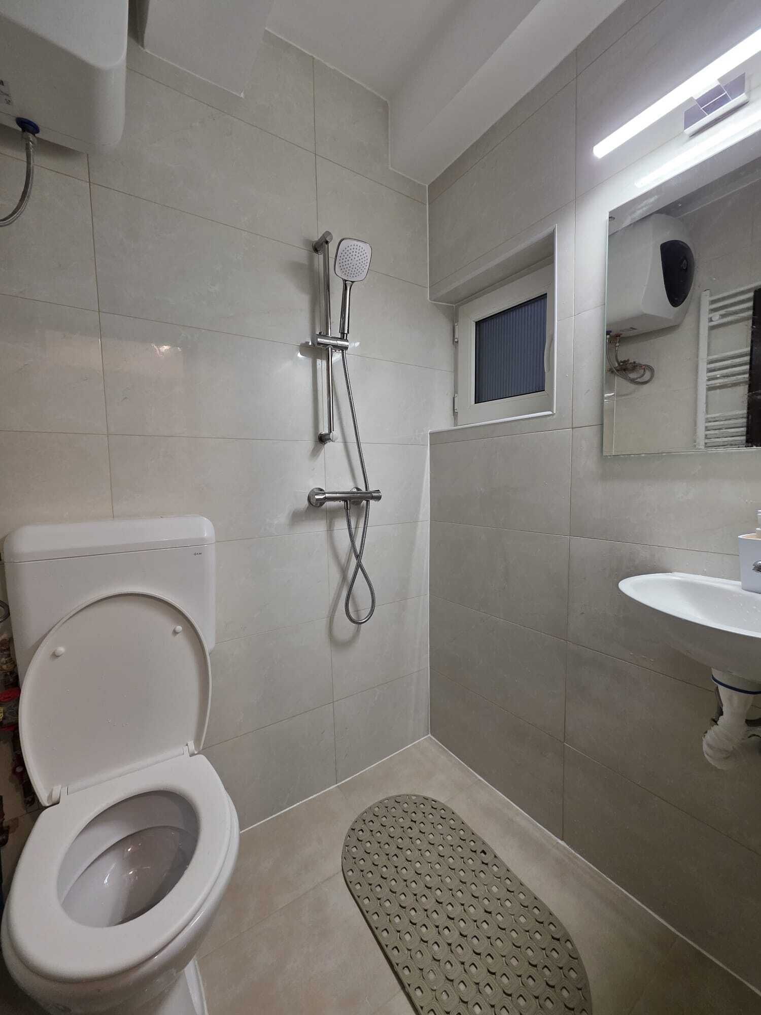 Une salle de bain avec des toilettes, une douche, un lavabo et une petite fenêtre.