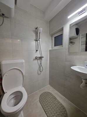 Een badkamer met toilet, douche, wastafel en een klein raam.