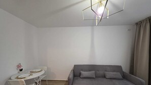 Ein Zimmer mit grauem Sofa, einem weißen Esstisch mit Stühlen und einer modernen geometrischen Leuchte.