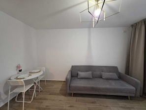 Ein Zimmer mit grauem Sofa, einem weißen Esstisch mit Stühlen und einer modernen geometrischen Leuchte.