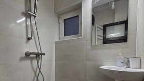 Ein Badezimmer mit Dusche, Waschbecken, Spiegel und kleinem Fenster.