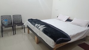 Un dormitorio con cama, dos sillas, una mesa y un enchufe.