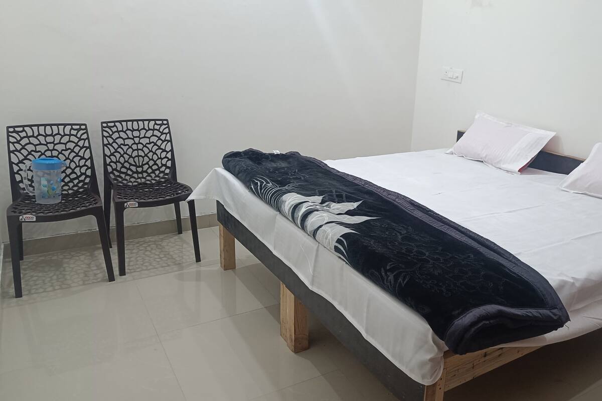A bedroom with a bed, two chairs, a table, and a wall socket.