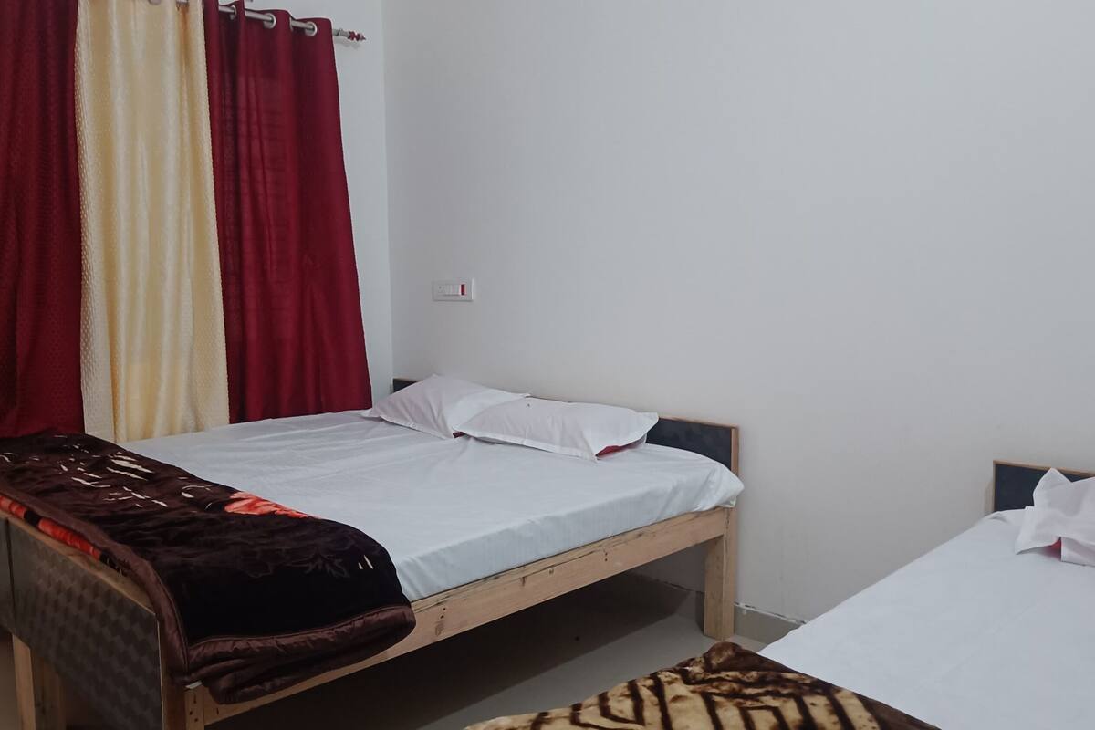 A single bed with a wooden frame, white bedding, and a dark patterned blanket.
