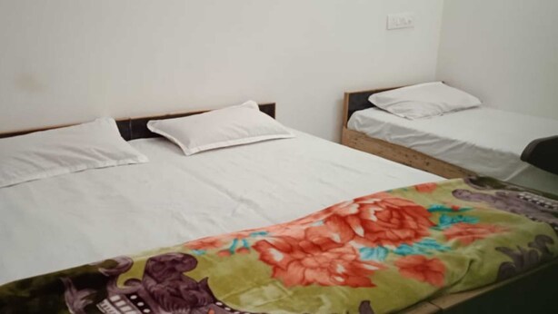 Dos camas individuales con ropa de cama blanca, un edredón floral en la cama inferior y una pared lisa con un enchufe.
