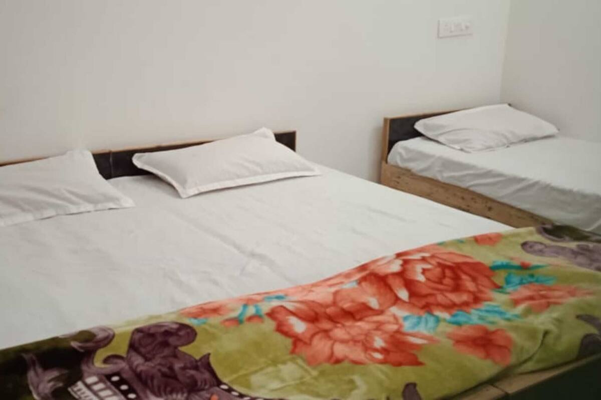 Two single beds with white bedding, a floral blanket on the lower bed, and a plain wall with a power outlet.