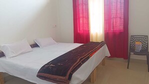 Una cama individual con ropa de cama blanca, un edredón marrón oscuro y una cortina roja que cubre parcialmente una ventana.