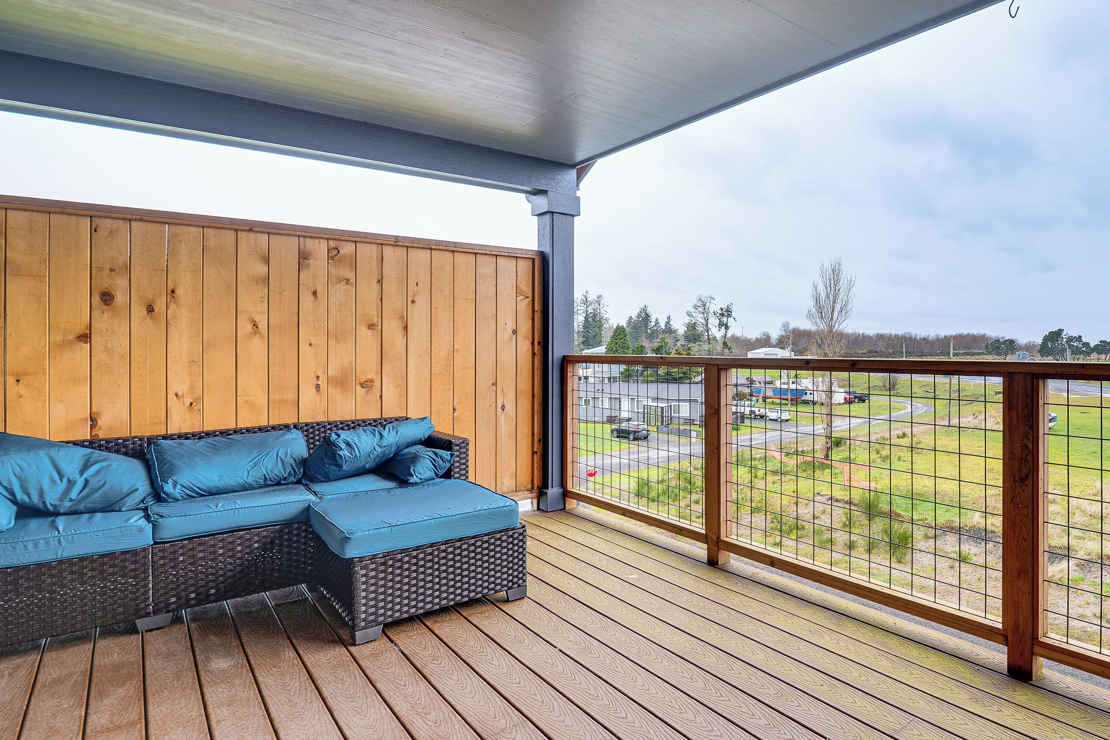 A covered outdoor seating area with a wooden wall, a cushioned bench, and a view of a parking lot.